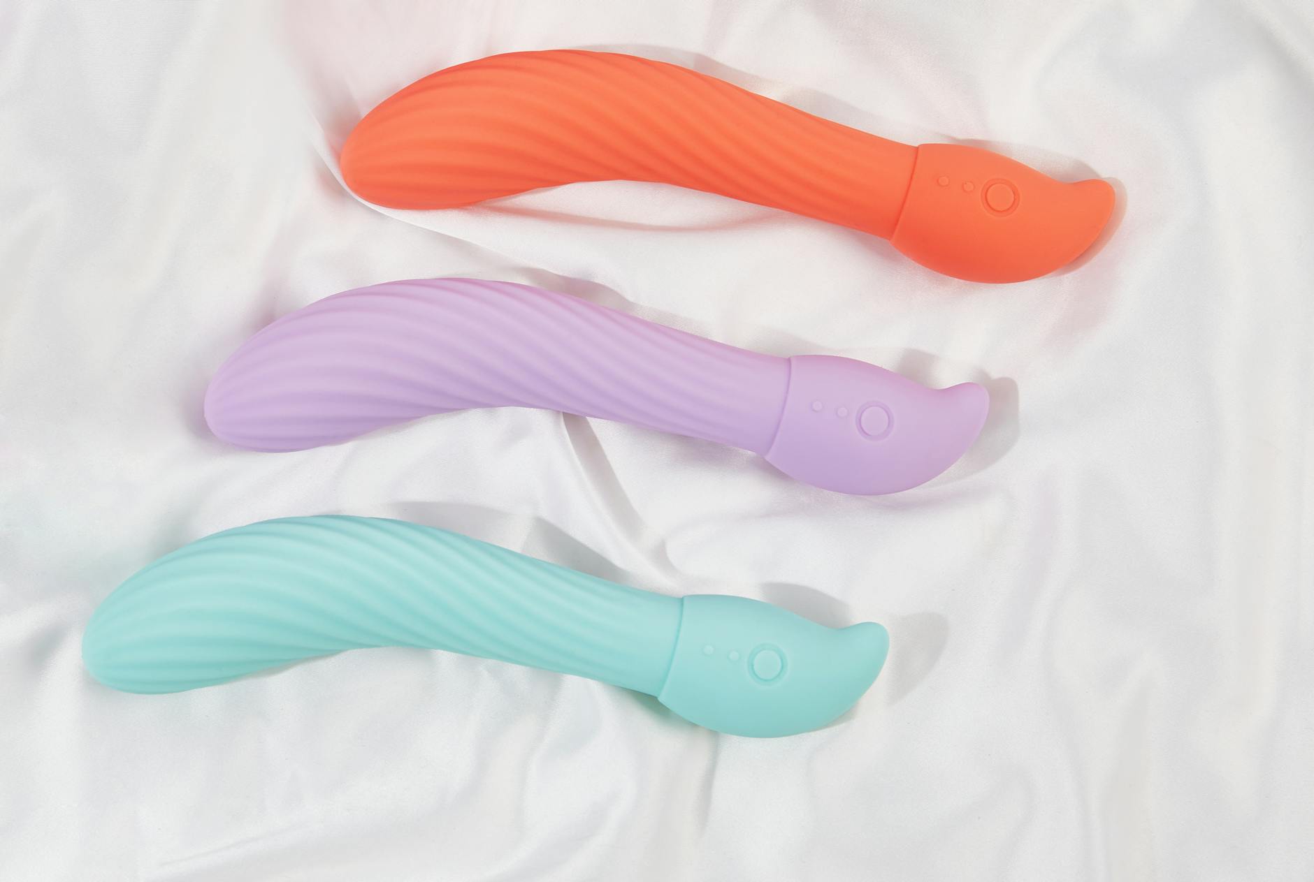 Eine Hand hält einen orangefarbenen Vibrator vor minimalistische violette Kulisse, zeigt moderne Sinnlichkeit