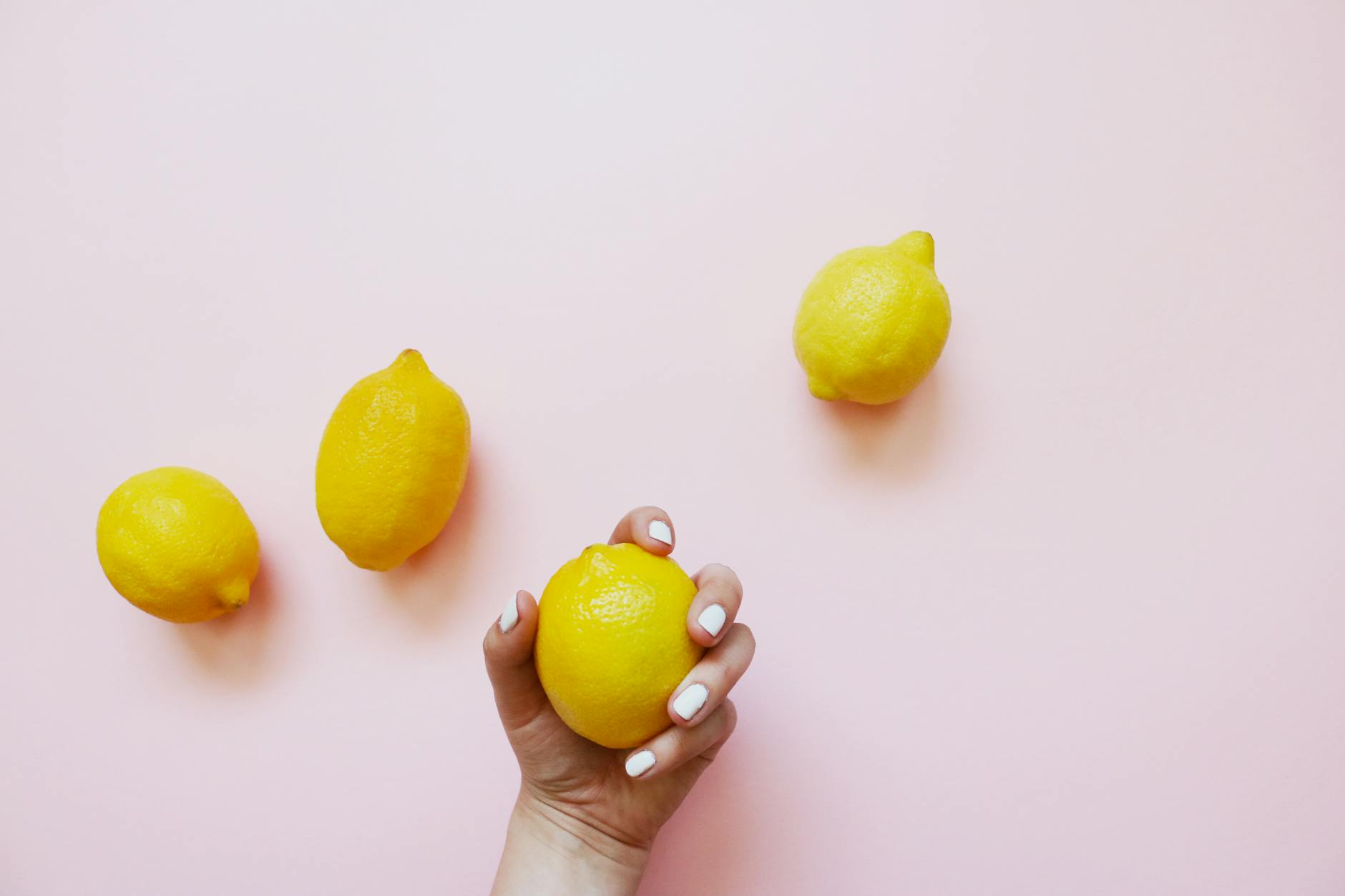 Hand holding a lemon on soft pink background symbolizing gentle, natural postpartum recovery