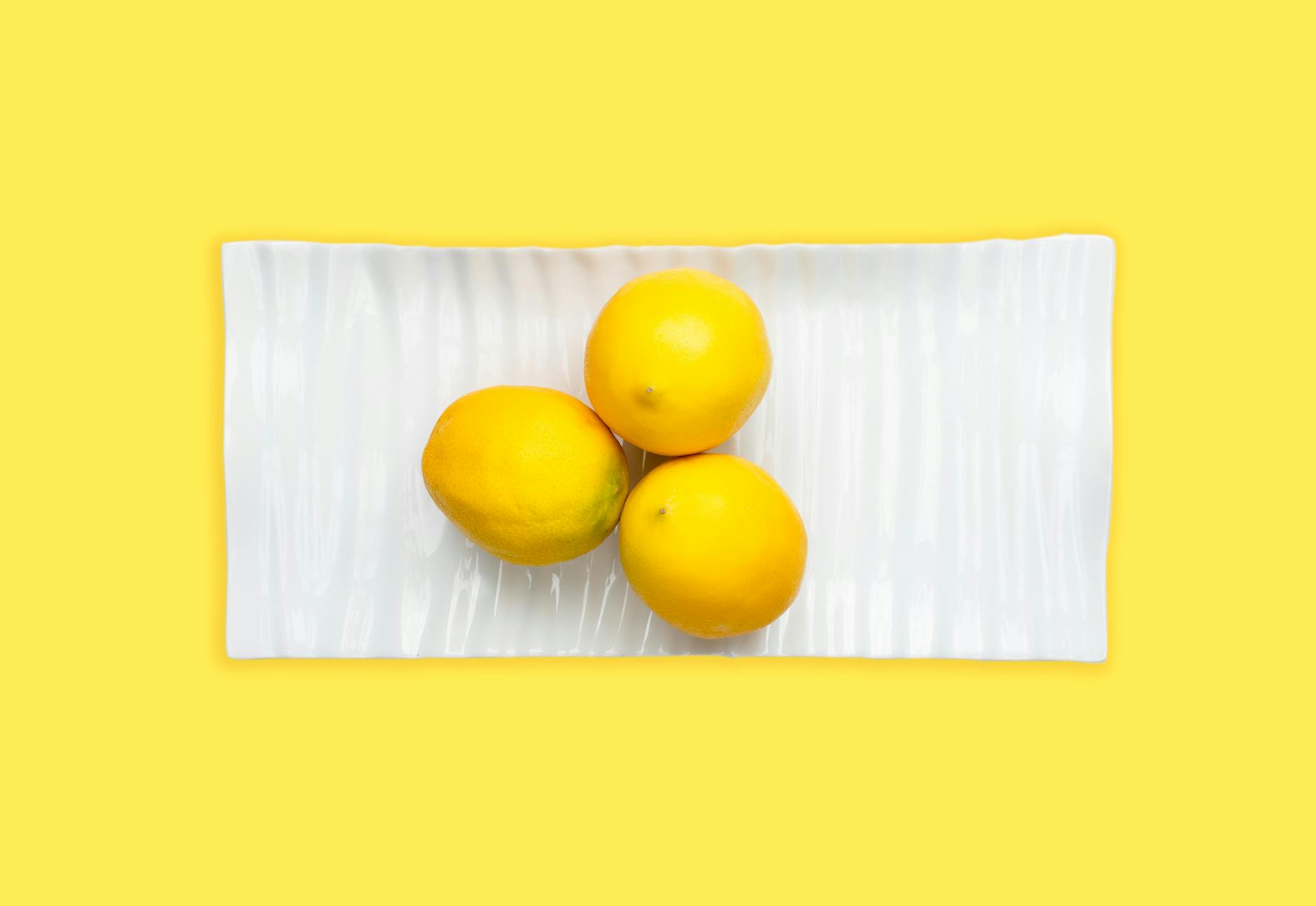 Hand holding a fresh lemon against a bright yellow background, symbolizing renewal and fresh sensation