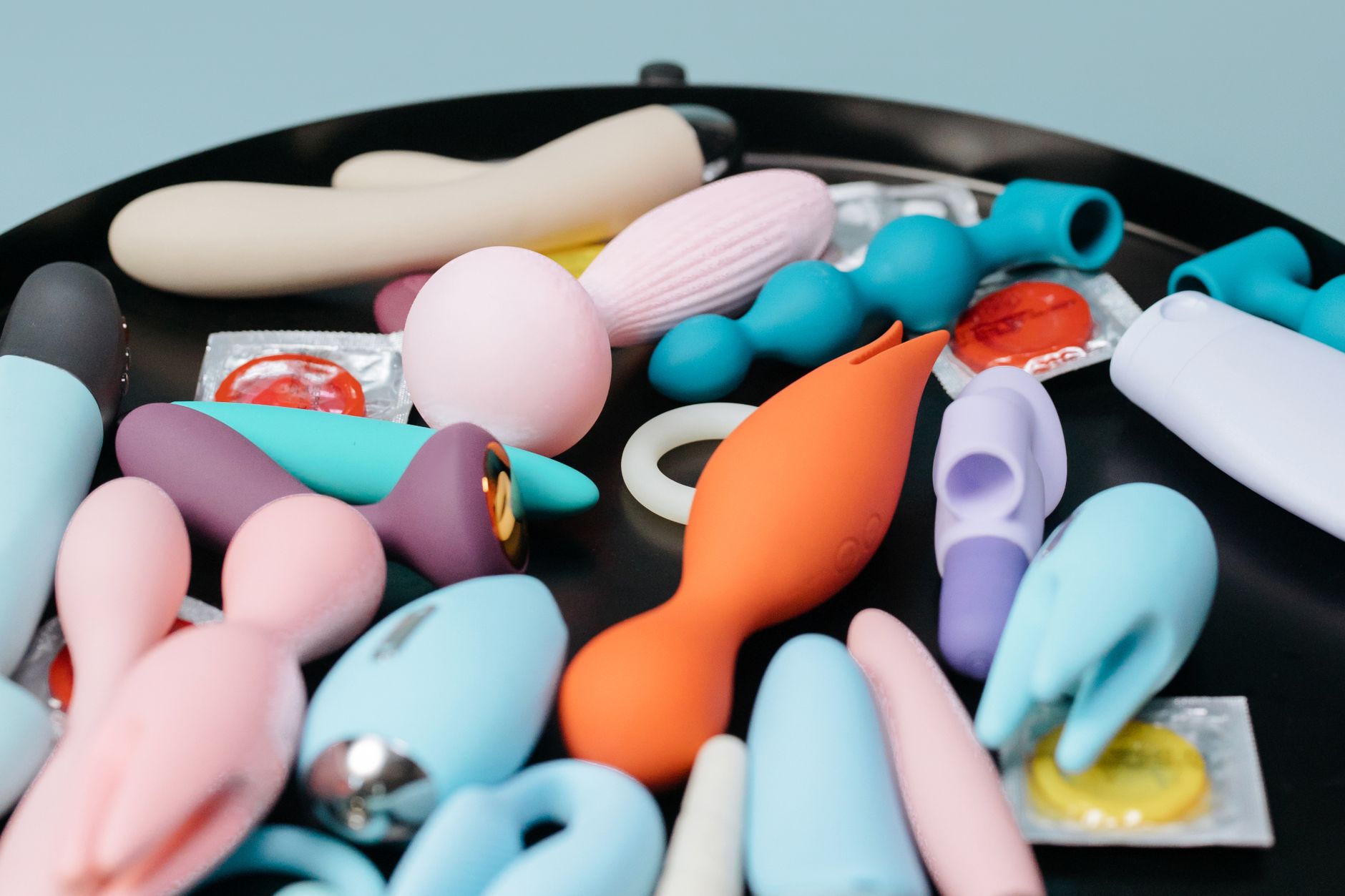 Eine Frau hält einen rosafarbenen Vibrator in der Hand, mit Kunstbüchern im Hintergrund, die intime und persönliche Themen betonen.