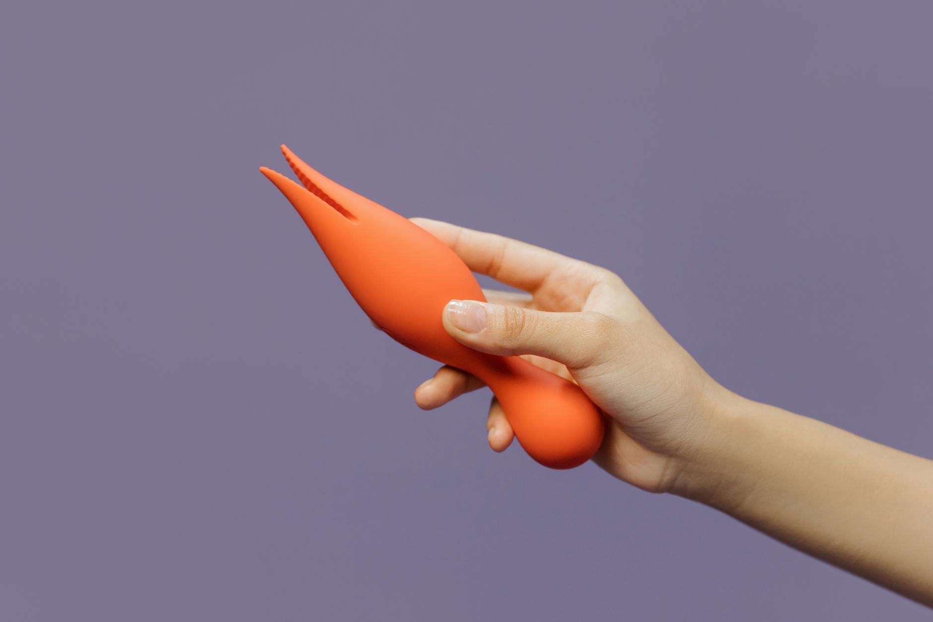 Hand hält einen orangefarbenen Vibrator gegen minimalistischen violetten Hintergrund, moderne Sinnlichkeit
