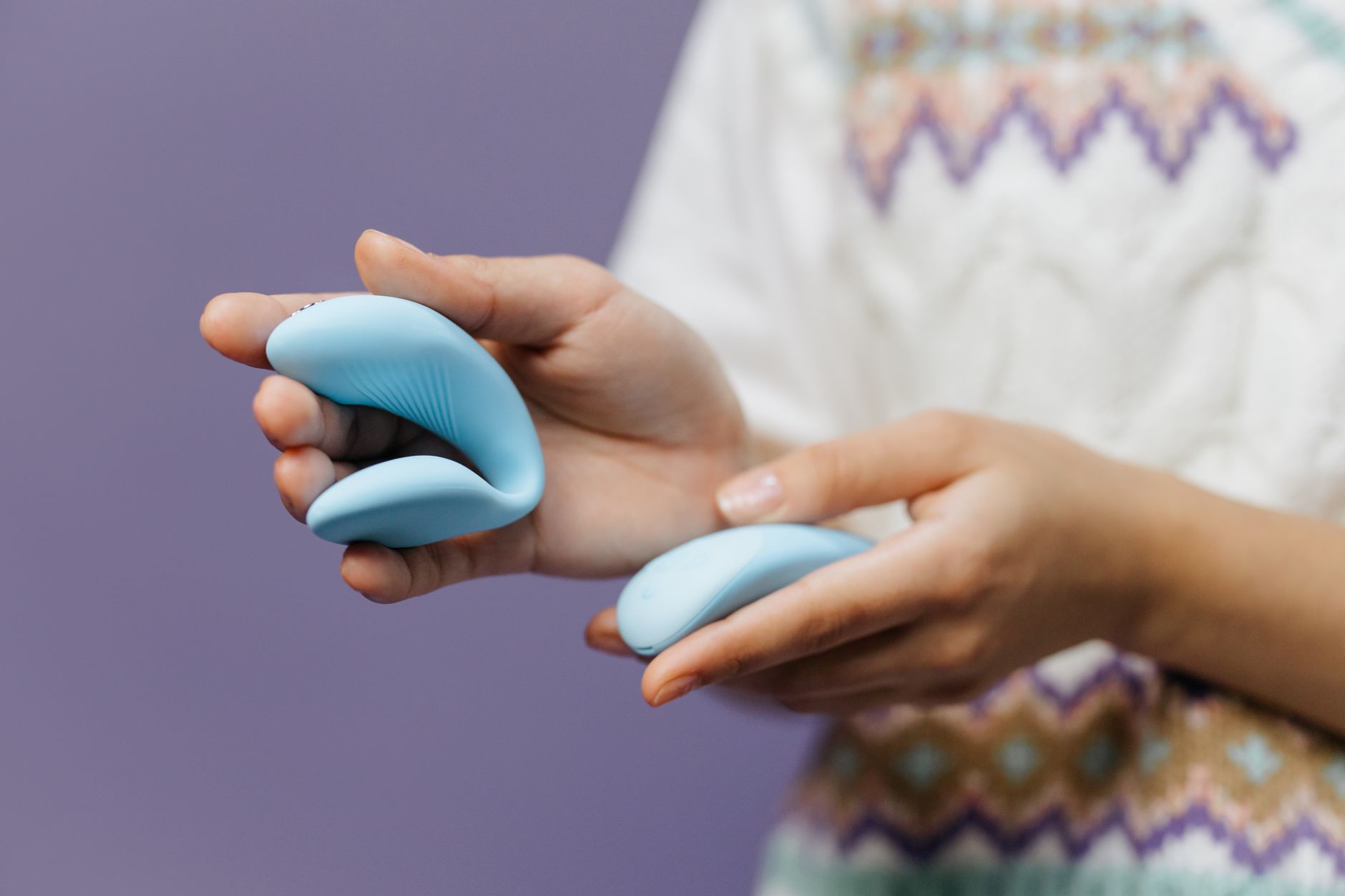 Nahaufnahme: Hand hält eleganten blauen Vibrator vor lila Hintergrund