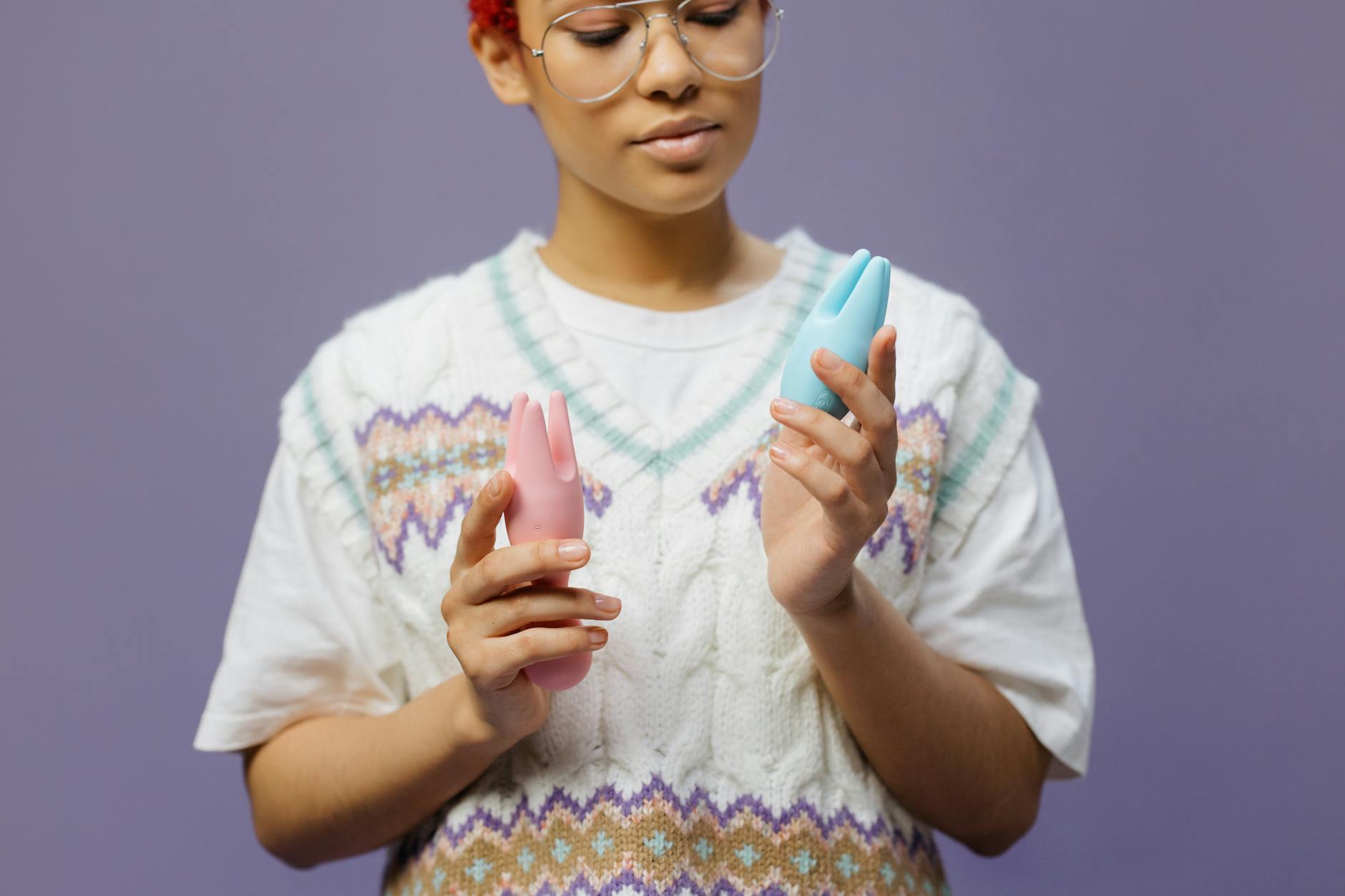 Hand holding an orange vibrator against a minimalistic purple backdrop