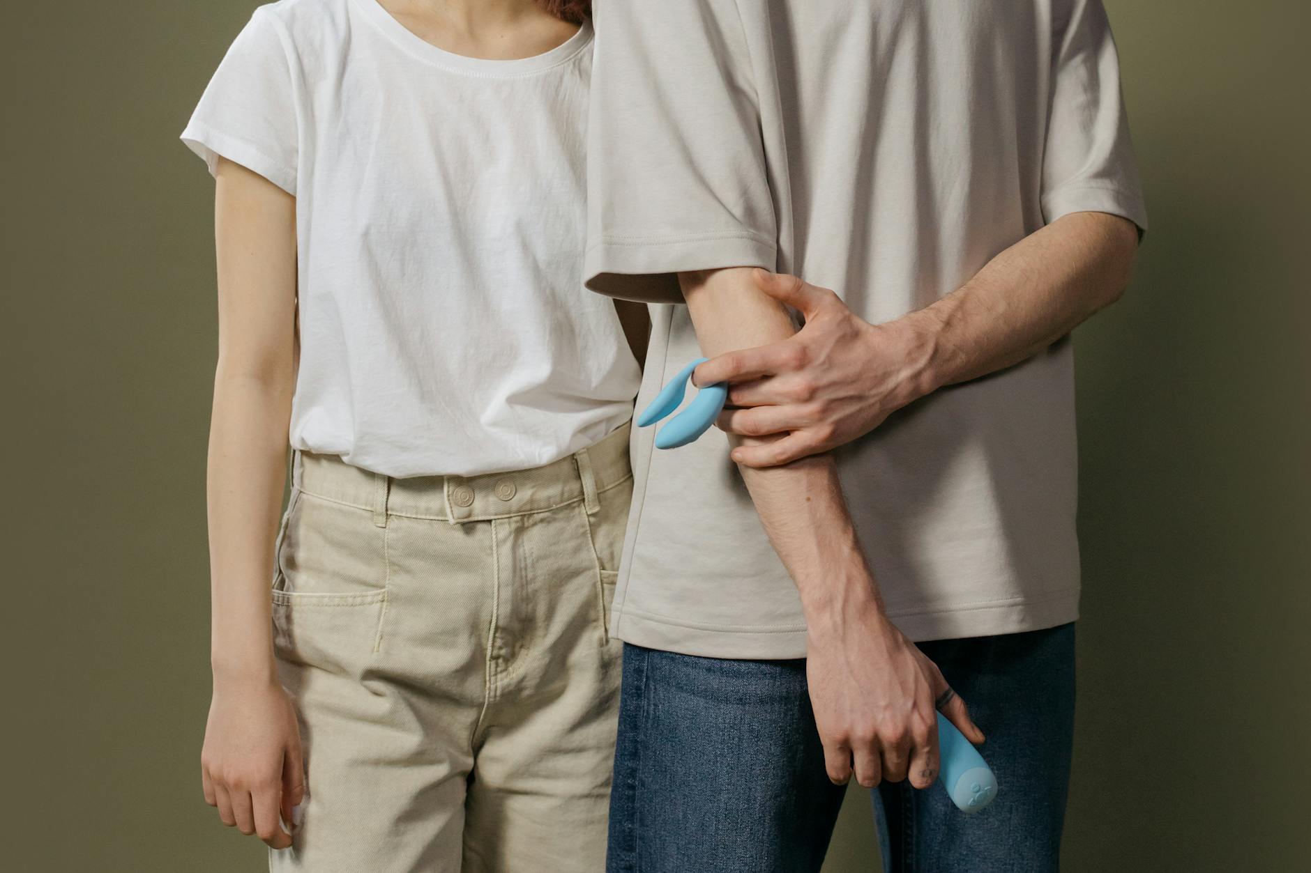 A young couple standing together indoors, holding a blue vibrator, symbolizing modern intimacy and permission.