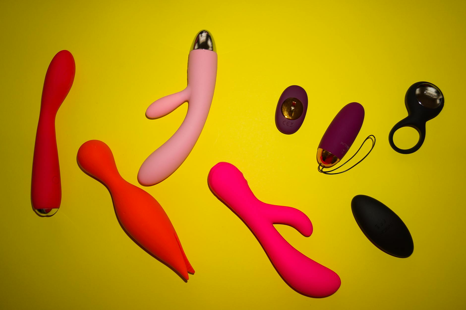 Nahaufnahme einer Hand, die einen orangen Vibrator gegen einen minimalistische lila Hintergrund hält