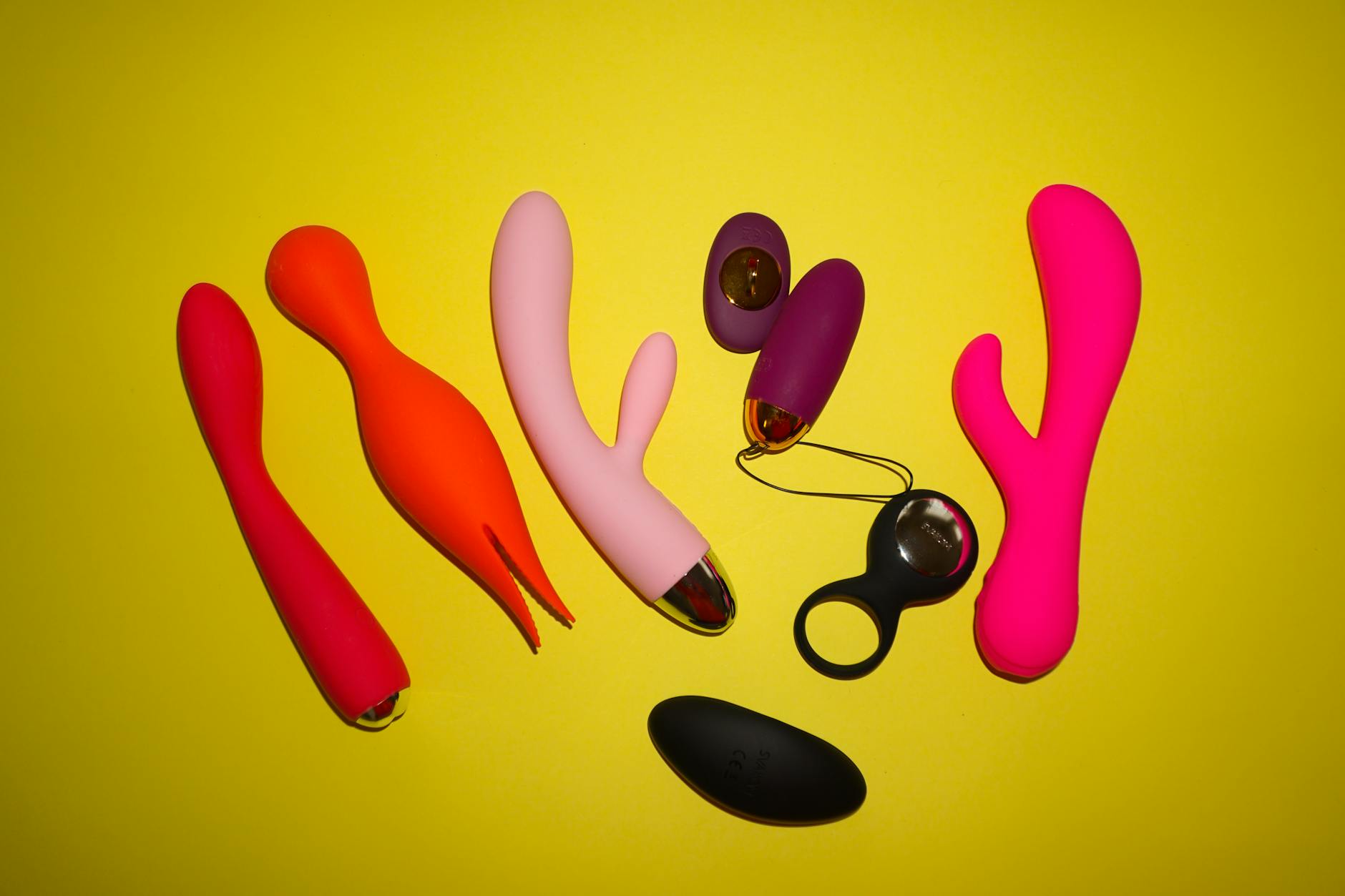 Two hands holding pink and blue clitoral vibrators against a soft pastel background